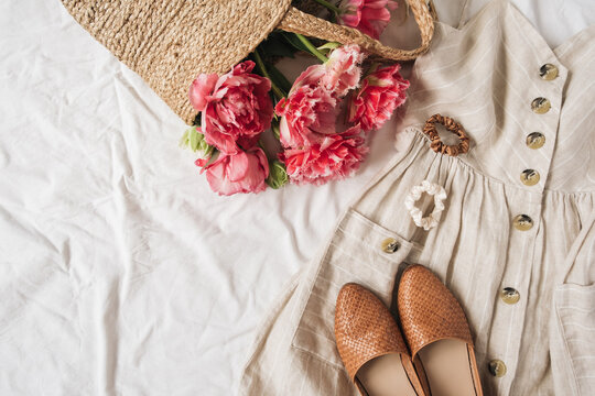 Beauty fashion collage with women's clothes and accessory on white linen. Sun dress sarafan, leather shoes, pink peony flowers in straw bag. Flat lay, top view fashion blog lifestyle concept