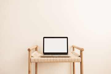 Laptop with blank screen on wicker bench against white wall. Minimal work / business / interior...