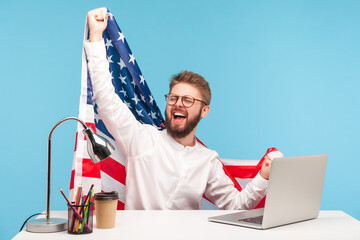 Extremely happy businessman raising American flag and yelling crazy for joy in office workplace,...