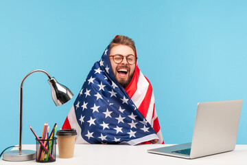 Extremely happy funny man employee sitting wrapped in American flag and shouting for joy in office workplace, celebrating labor day or US Independence day 4th of july, government employment support. - Powered by Adobe