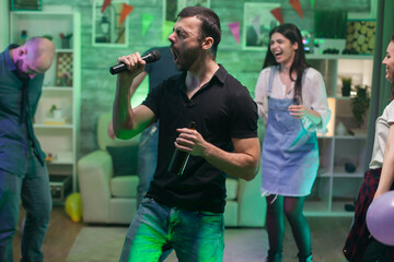 Naklejka premium Bearded male singing a rock song on microphone while partying with his friends.
