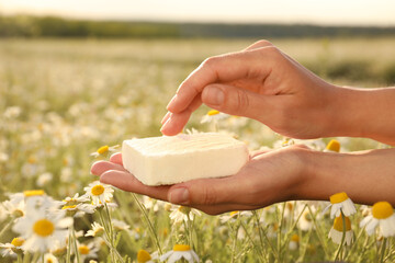 Woman holding natural soap in chamomile field, closeup