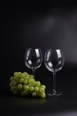 Still life on a black background. A glass wine glass and grape vine.