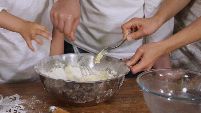 Children helping parents to preparing a dough in domestic kitchen. Close-up hands of happy big family is kneading a dough in steel bowl together at home.
