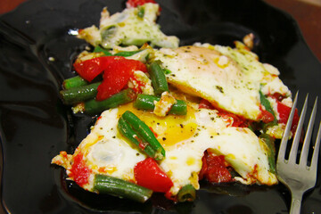Morning roasted whole eggs on the black plate and with tomato and green beans