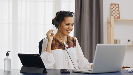 Happy business woman wearing headphone during a video call while working from home office.
