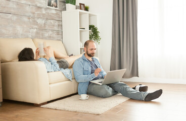 Couple relaxing in living room reading and browsing on internet.