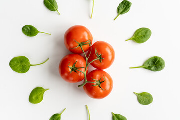 Sprig of fresh red juicy tomatoes in the center and leaves of spinach around it on a white table. Vegeterian food. Top view. Close-up