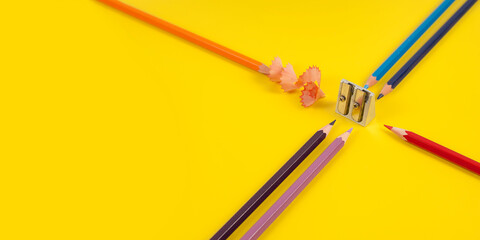 Some colored pencils of different colors and a pencil sharpener and pencil shavings on а yellow background