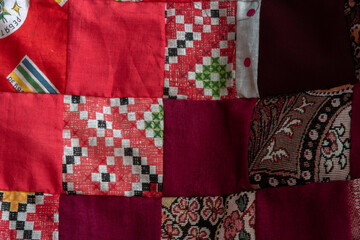 Red patchwork quilt fragment. Colorful handmade ethnic blanket. Worn clothes reuse concept.