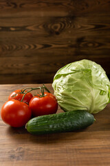 Fresh cabbage, tomatoes and cucumber on a brown wooden table. Vegetarian food. Healthy eating. Vertical 
