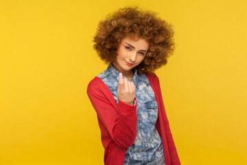 Come here, follow me! Portrait of pretty curly-haired woman looking playfully and calling with one finger, making beckoning gesture, inviting to come. indoor studio shot isolated on yellow background