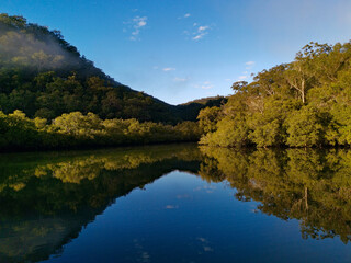 Fototapeta na wymiar Beautiful morning view of Cockle creek with reflections of blue sky, foggy mountains and trees, Bobbin Head, Ku-ring-gai Chase National Park, New South Wales, Australia