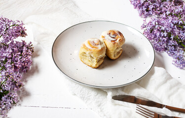 Cinnamon roll or cinnabon with white cream glaze on plate on white wooden background. Traditional homemade sweet buns.