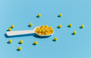 A white spoon filled with yellow vitamin C tablets on a blue background. Prevention of colds and flu