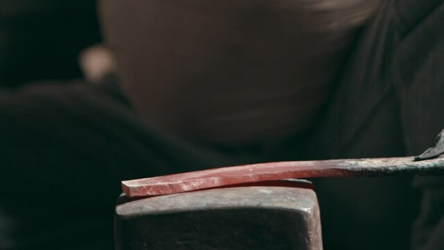 Hands of a rural blacksmith hammering a metal piece on an anvil