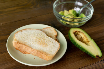 Fried bread for toasts and avocado for breakfast in the morning on brown woodwn table on green background. 