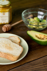 Fried bread for toasts, avocado and honey for breakfast in the morning on brown woodwn table on green background. Vertical