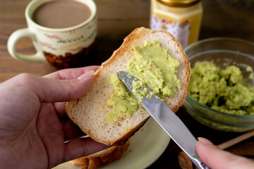Female hand cooking fresh tasty toasts with avocado and honey and  a cup of coffee for breakfast on brown wooden table. 