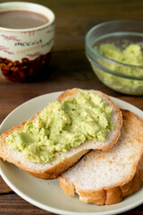 Fresh tasty toasts with avocado and a cup of coffee for breakfast on brown wooden table. Vertical. 