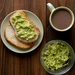 Tasty toasts with avocado and a cup of coffee for breakfast on plate on brown wooden table. Vertical. Top view