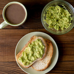 Tasty toasts with avocado and a cup of coffee for breakfast on plate on brown wooden table. Vertical. Top view