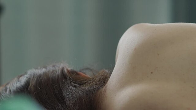 Rear view of attractive young caucasian woman lying on her side on bed. Close up of female bare back. Beautiful brunette woman with long hair sleeping in the morning.