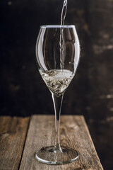 Pouring white wine in glass on the rustic wooden background. Selective focus. 