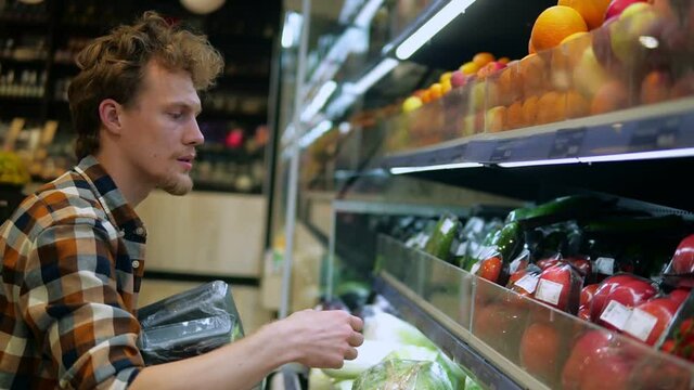 A caucasian man in plaid shirt shopping for fruits and vegetables in produce department of a grocery store supermarket. Choosing perfect fresh tomatoes from the lower shelf. Side view