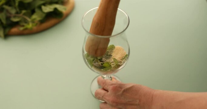 Mashing mint and sugar in glass with muddler to make mint mojito coffee