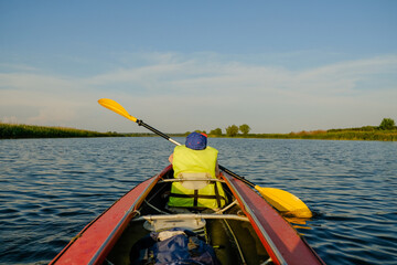 A little boy kayaks on the river in the summer and rowing an oar.