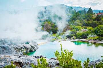 Thick steam gothering over turquoise water of a geothermal lake in the mountains