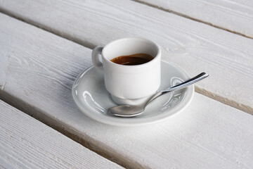Espresso italian coffee in a simple white cup on a wooden planks painted on white background or backdrop.