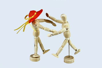 Pair of wooden mannequins, she with orange straw hat, running towards each other. Light background.