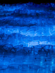 huge heap of thrown away used transparent disposable plastic cups illuminated by blue light, environmental pollution
