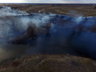 Fototapeta na wymiar The smoke from the burning of dry grass (drone image).Local residents set fire to the grass specifically. Small animals are bending. Local features and habits. Near Kiev,Ukraine