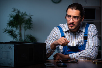 Young male technician repairing computer in workshop at night