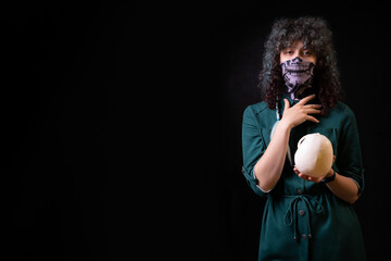beautiful young curly girl on a black background in a mask is surprised, posing and holding a skull in her hands