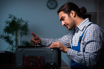 Young male technician repairing computer in workshop at night