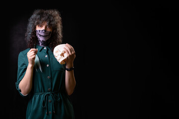 beautiful young curly girl on a black background in a mask holds a tooth, part of the skull
