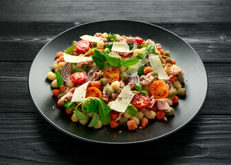 Mini potato gnocchi tricolour with tomato, spinach, Seasonal salad leaves and parmesan cheese on black plate