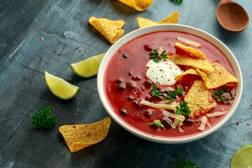Mexican Chilli bean soup with yogurt, cheese, lime and tortilla chips in white bowl