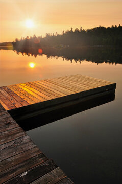Sun rising over the still water of Lake Temagami, Ontario with a deck in the foreground.