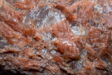 Photograph of a granite surface interspersed with transparent mica in soft focus at high magnification. Fine texture of natural mineral of pink color with blurred background.