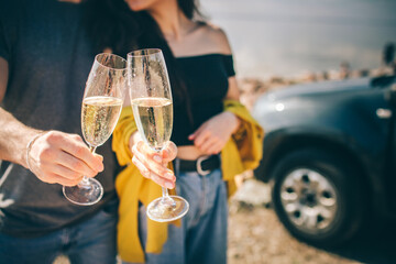 Travel, tourism - Man and woman drink champagne near the water at a folding portable table. Picnic near the water. Couple going on Adventure. Car travel concept.