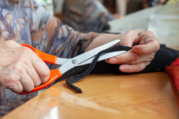 Hands of an elderly woman cut the fabric. Cutting fabric closeup. Dressmaker at work. Tailoring.