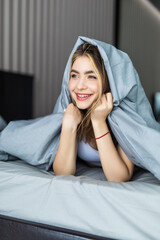 Smiling young girl under a duvet in her bedroom