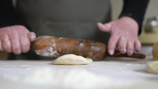 An adult woman rolls dough in her kitchen to prepare baking or dumplings, manti