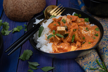 Vegan Thai red curry with tofu and sweet potatoes served in black bow on blue table. Copy space.