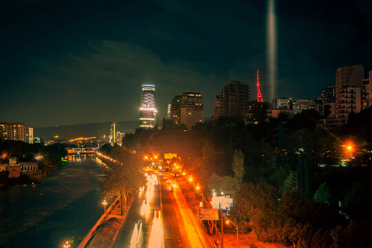 Traffic in city at night with dark river and column of the light in a distance © TOMASZ